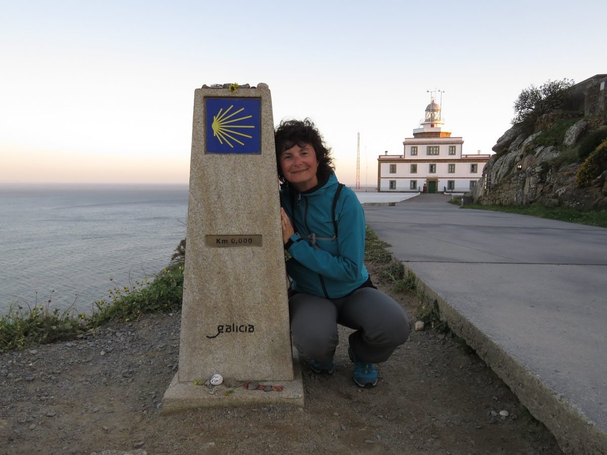 Elisa Semeghini accanto al cippo del chilometro zero a Finisterre, in Galizia, con il faro sullo sfondo